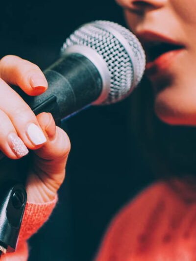 Singer at microphone. Woman singing and holding mic. Female vocal talent. Music show recital.